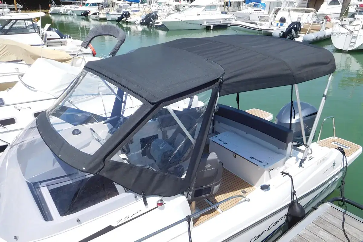 Un bateau blanc avec un taud neuf, prêt à naviguer. Le taud de bateau est noir, protégeant le cockpit et le pare-brise.