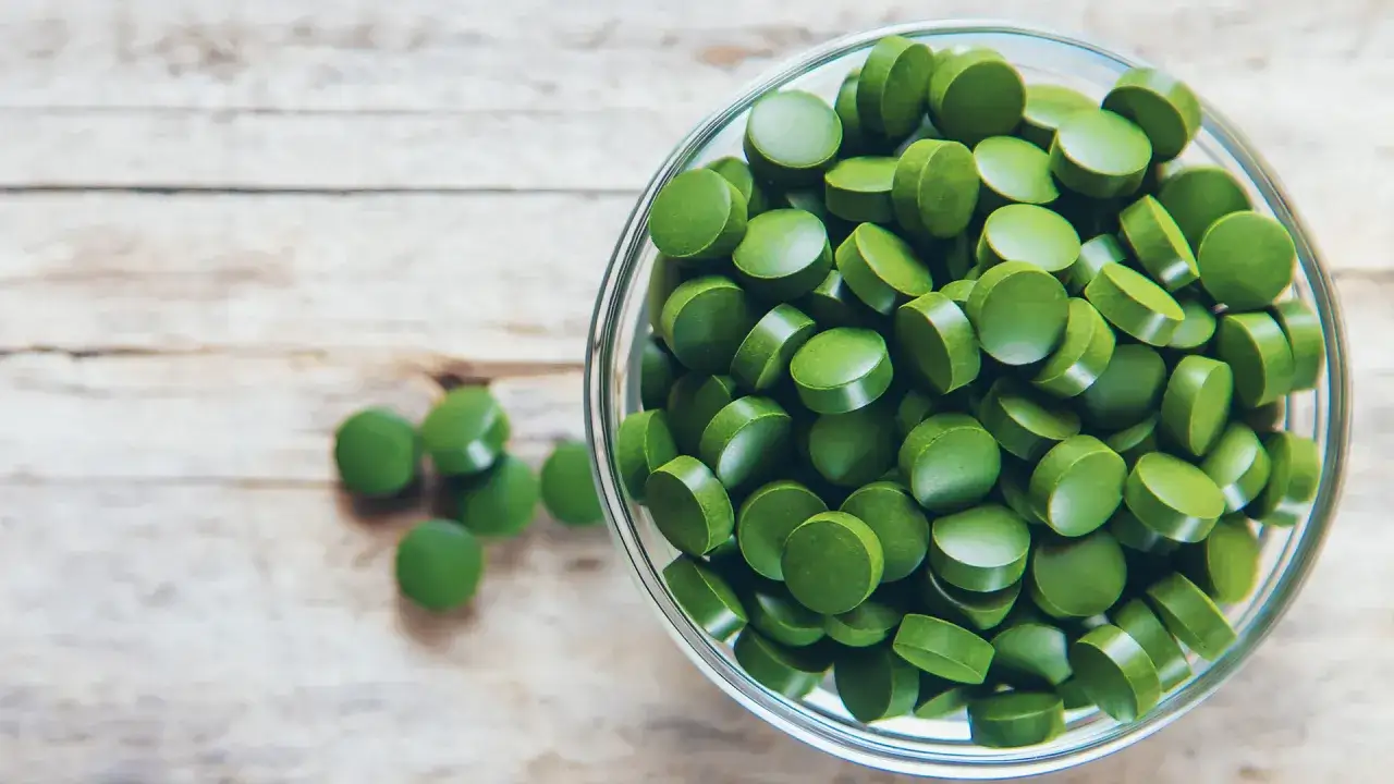 Grüne Chlorella-Tabletten in einer Schüssel. Manche Menschen berichten über leichte Chlorella Nebenwirkungen wie Verdauungsbeschwerden.