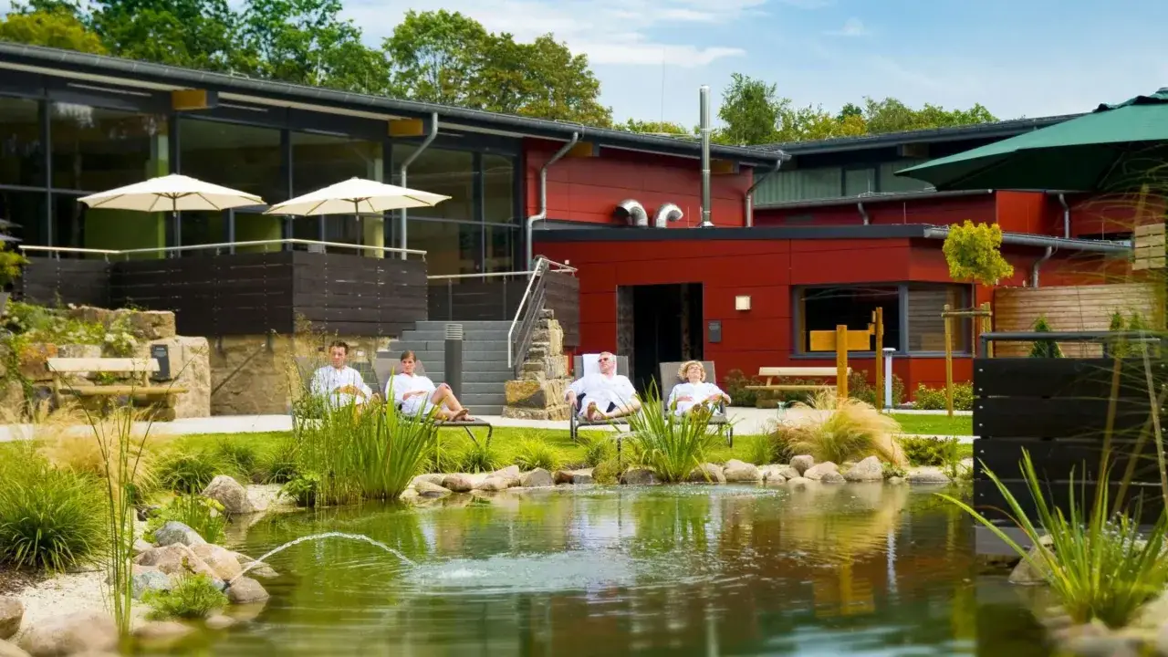 Entspannte G&auml;ste in wei&szlig;en Roben ruhen sich am Teich der Olsberg Therme aus.