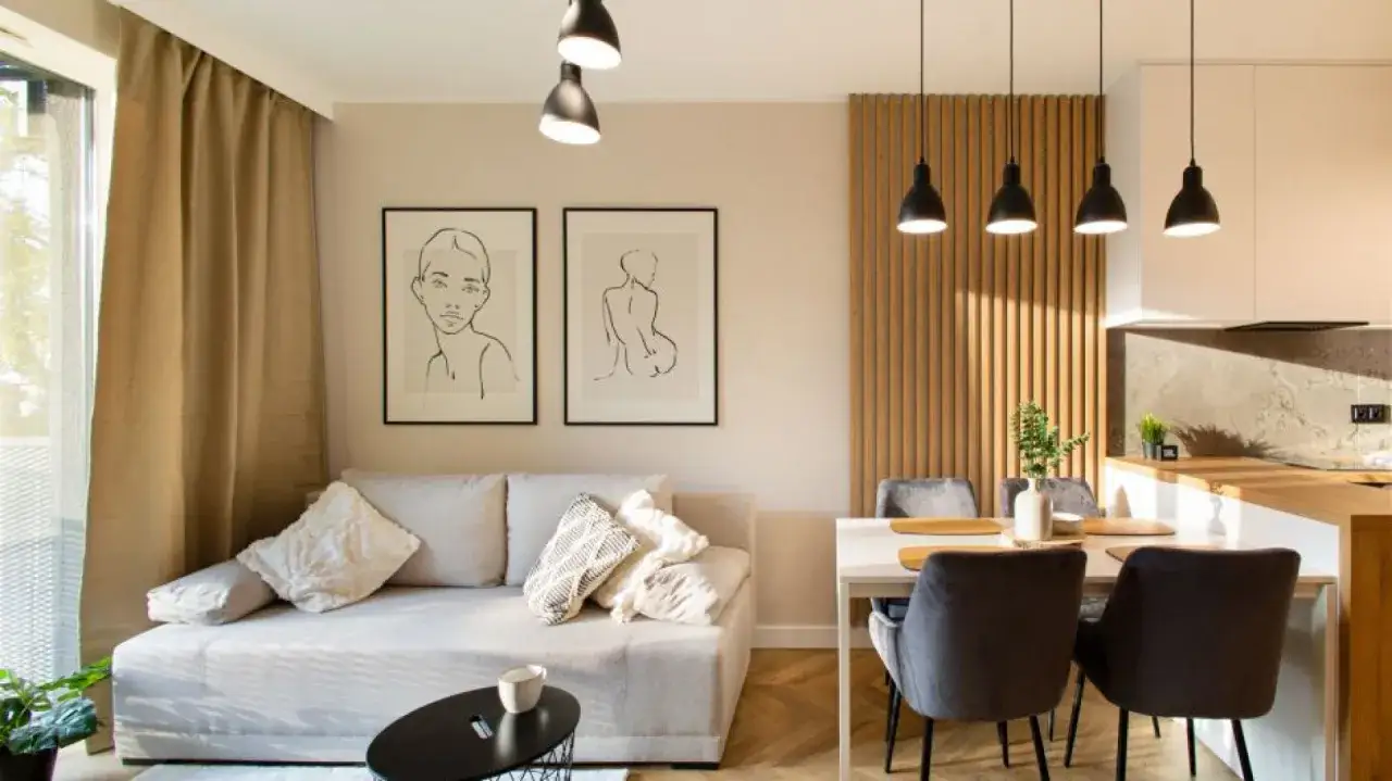 Jasny salon z sofą i dwoma obrazami na ścianie. Kolor piaskowy na ścianie tworzy przytulną atmosferę.
