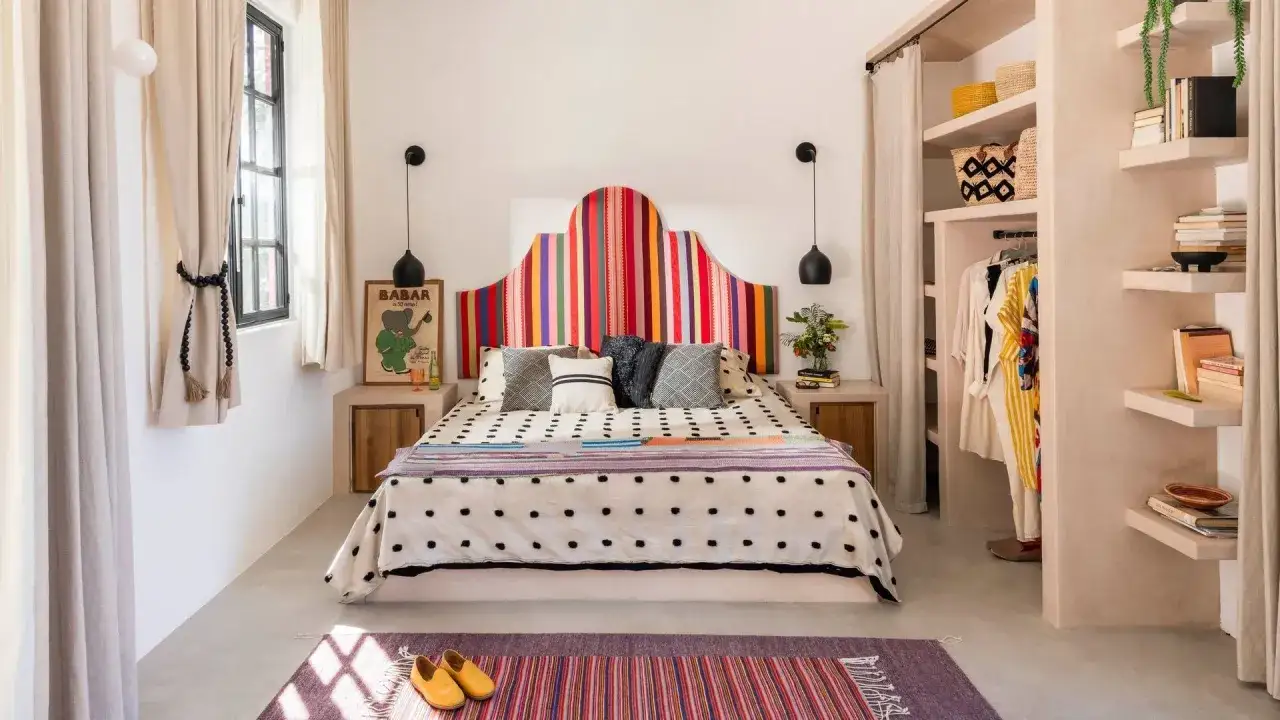 A vibrant, arched headboard with colorful vertical stripes offers unique headboard ideas. The bed is adorned with patterned pillows and a polka-dot duvet.