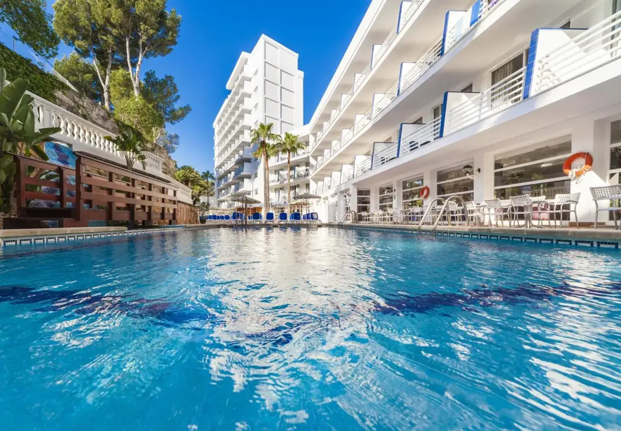 Basen hotelowy z leżakami i palmami przy nowoczesnym budynku. Idealne miejsce na wakacje w Globales Palmanova Palace.