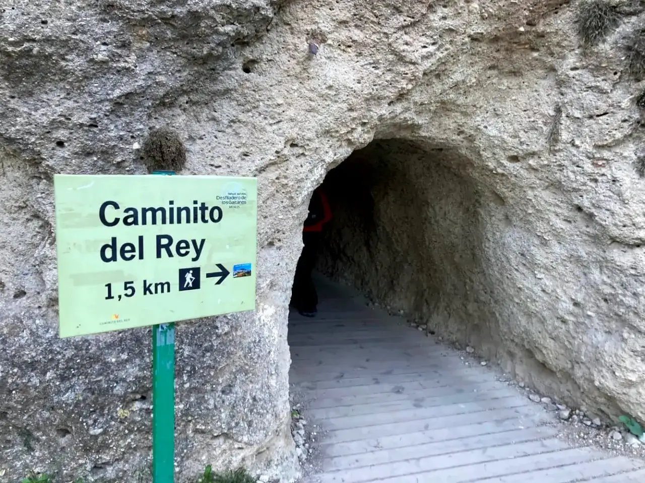 Schild am Caminito del Rey alter Weg weist den Weg durch einen Felsentunnel mit Holzstegen.