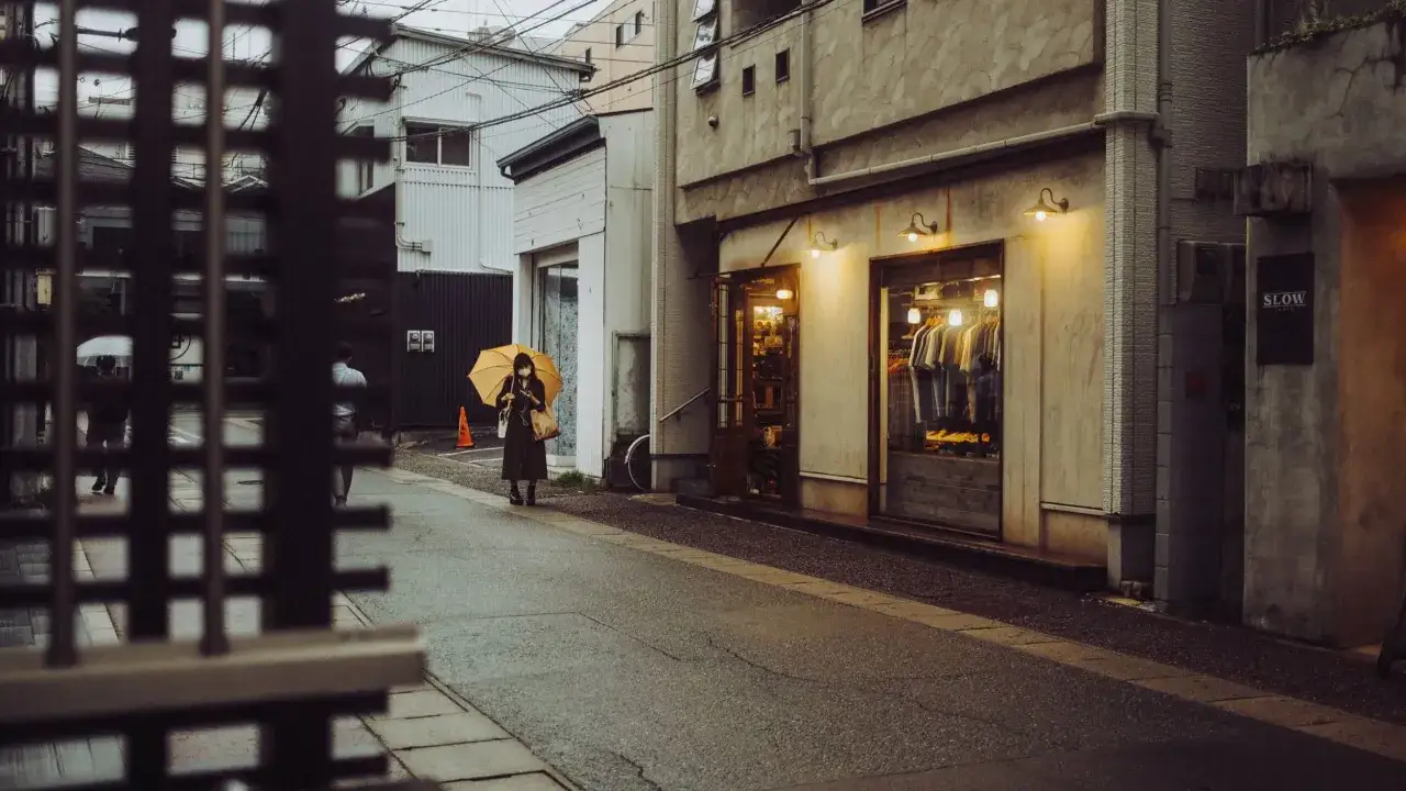 Una mujer con paraguas amarillo camina por una calle de Jap&oacute;n. Fujifilm X100V fotos capturan la atm&oacute;sfera urbana.