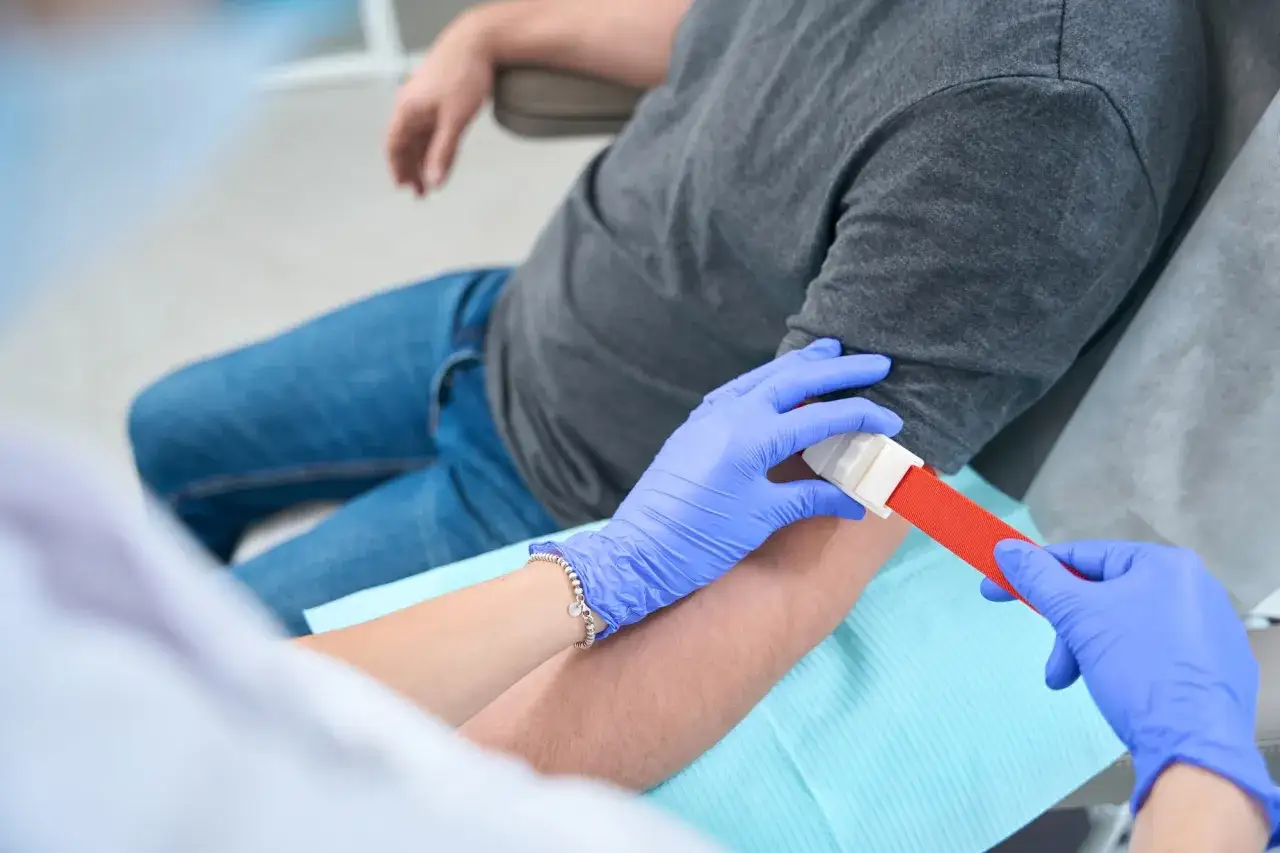 Pielęgniarka zakłada opaskę uciskową na ramię pacjenta przed pobraniem krwi. To ważny krok w badaniach kontrolnych, kt&oacute;re pomagają dbać o moje zdrowie.