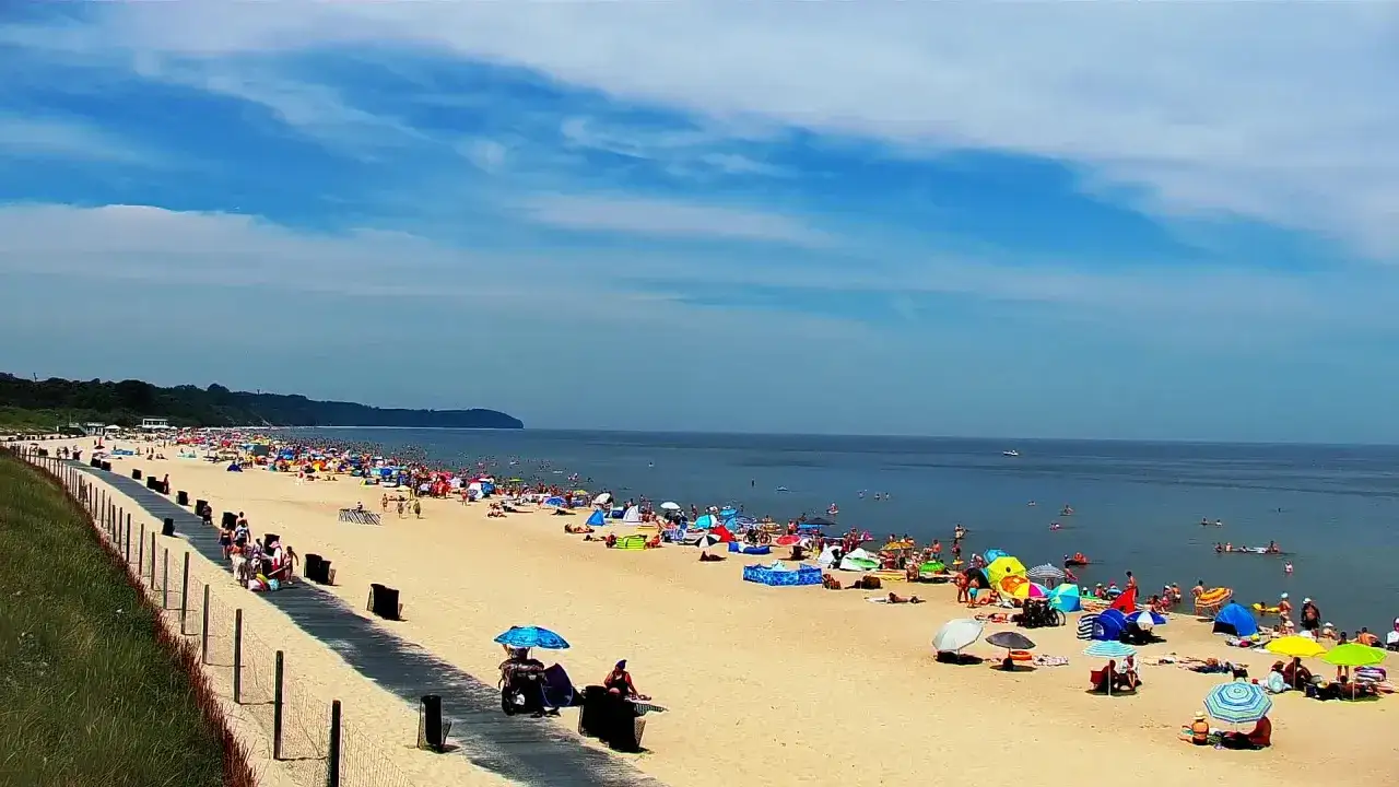 Tłum ludzi na plaży, z parasolami i parawanami, woda i niebo. Widok z Gdyni na Władysławowo.
