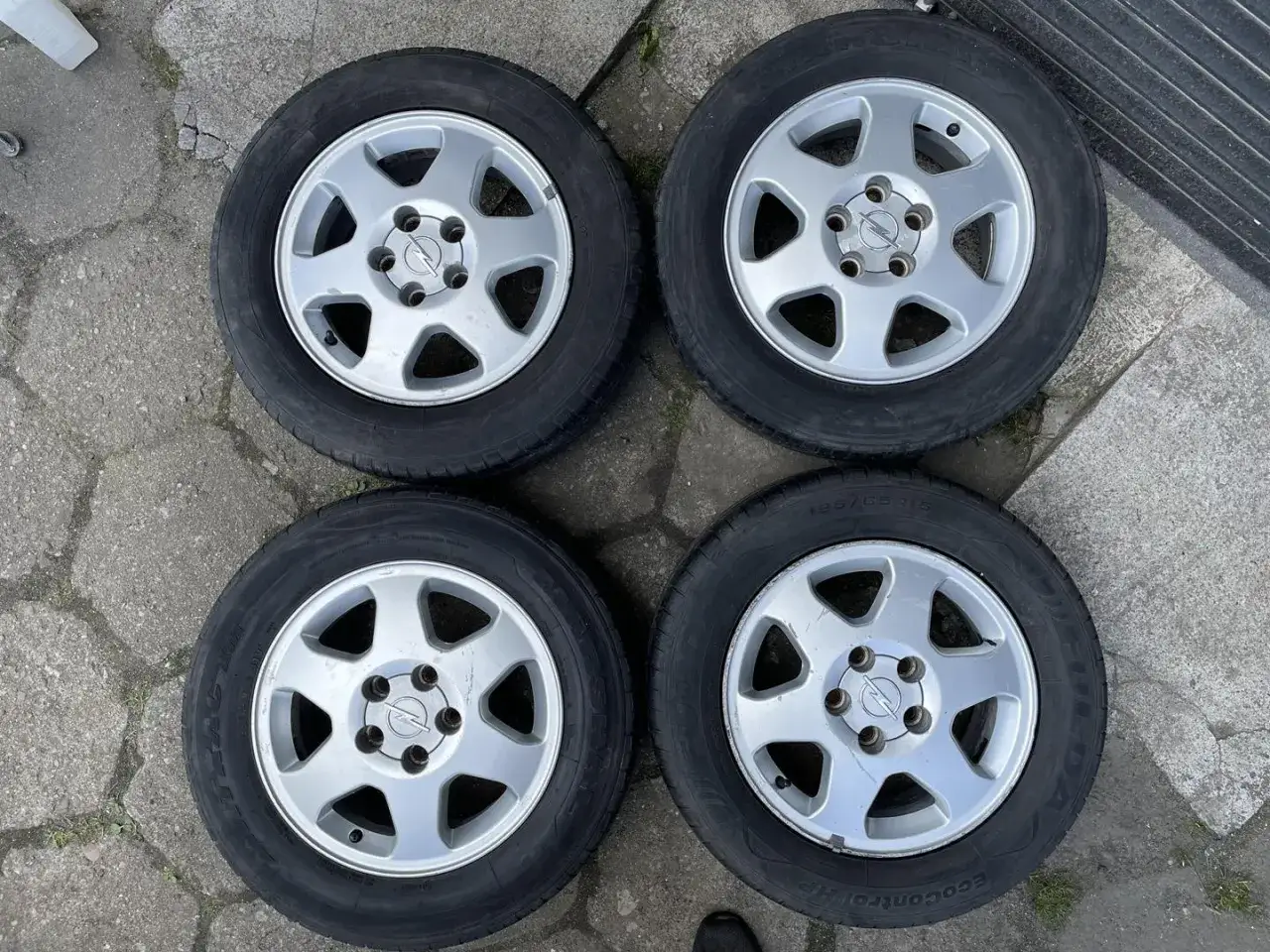Cztery felgi aluminiowe do Opla Astry H, z widocznym rozstawem śrub.