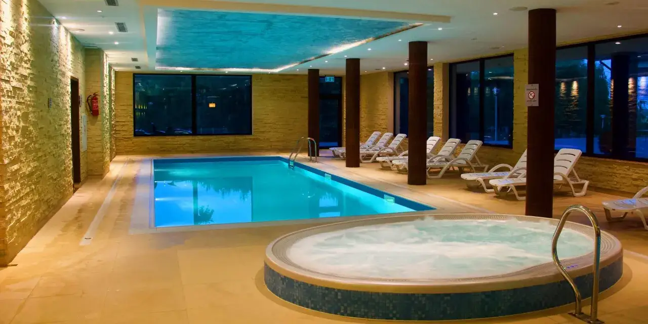 Relaks w basenie i jacuzzi w Mikołajki Resort Spa. Jasne płytki, kamienne ściany i wygodne leżaki tworzą atmosferę spokoju.
