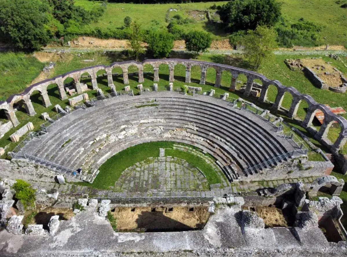Antico teatro romano, con gradinate in pietra e un'area verde centrale. Le arcate in rovina circondano il **teatro viterbo**, immerso nel verde.