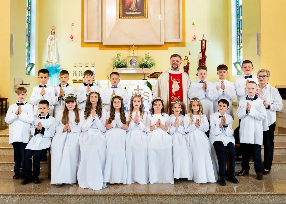 Dzieci w białych strojach komunijnych z księdzem i rodziną w kościele. Ile trwa komunia w kościele? Zwykle około godziny.