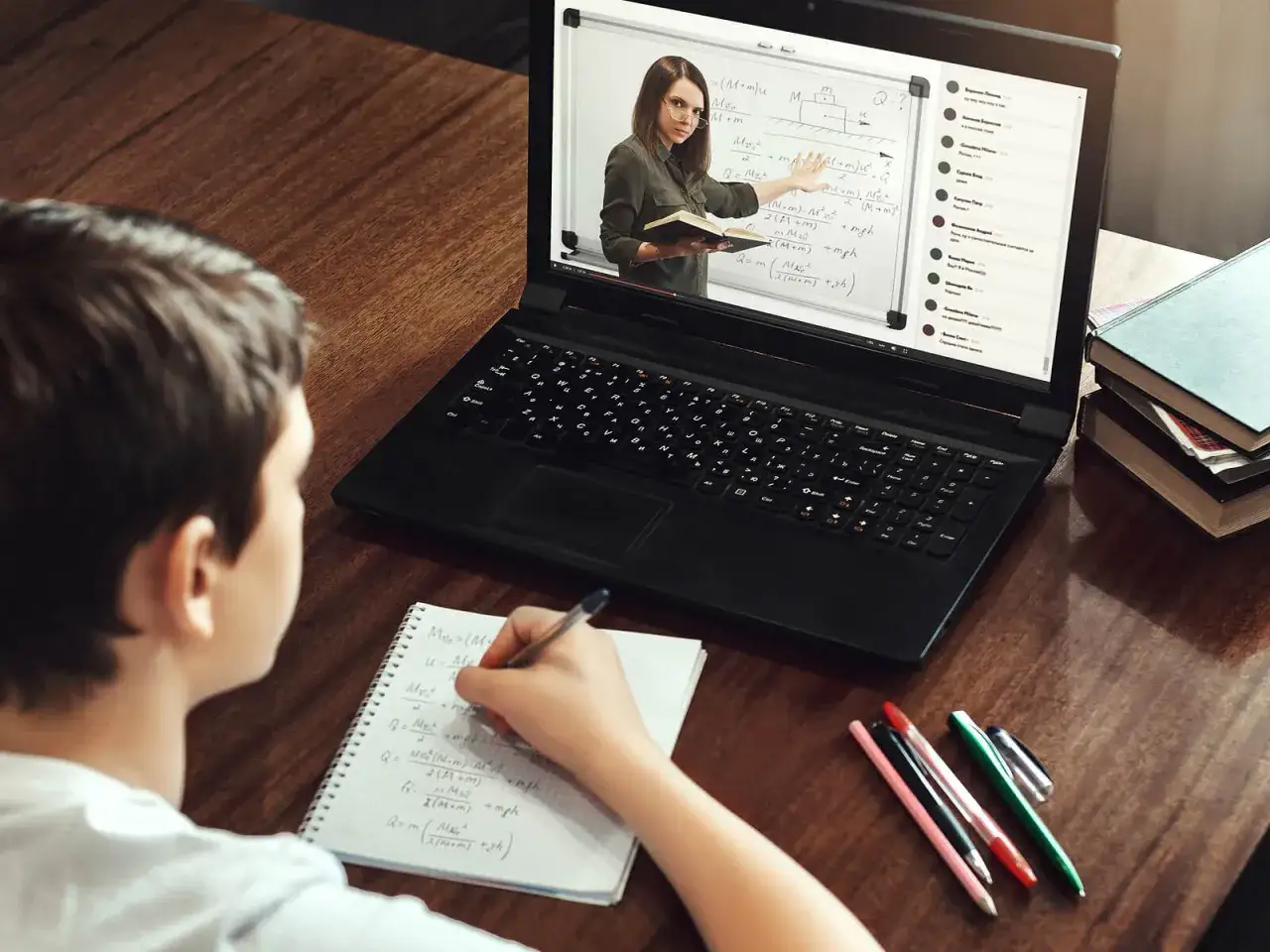 Un ni&ntilde;o estudia en l&iacute;nea, tomando notas mientras una profesora explica f&iacute;sica en la pantalla.