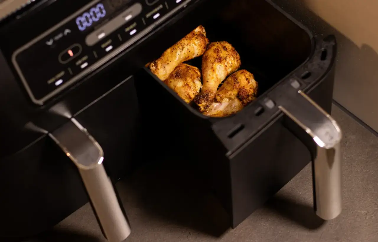Czy air fryer jest rakotwórczy? W koszu urządzenia pieką się złociste udka kurczaka.