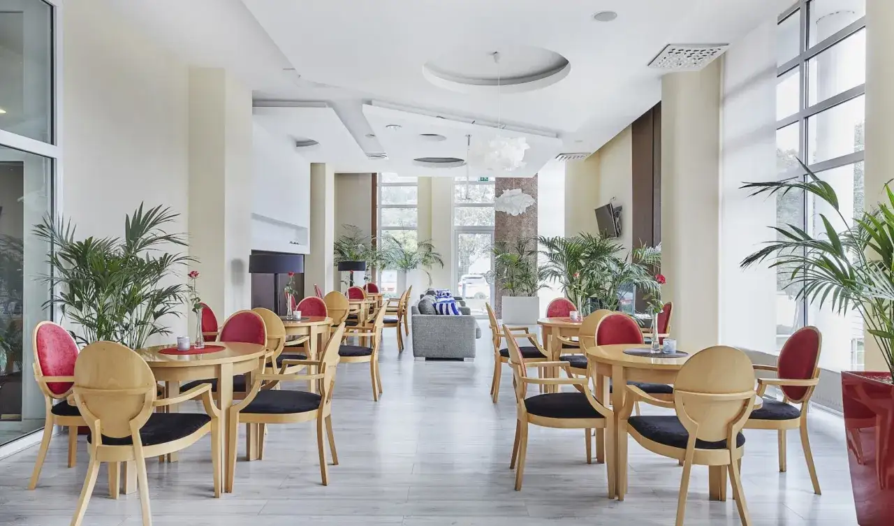 Przytulna jadalnia w hotelu Diva Kołobrzeg. Jasne drewno, czerwone obicia i mnóstwo zieleni tworzą relaksującą atmosferę.