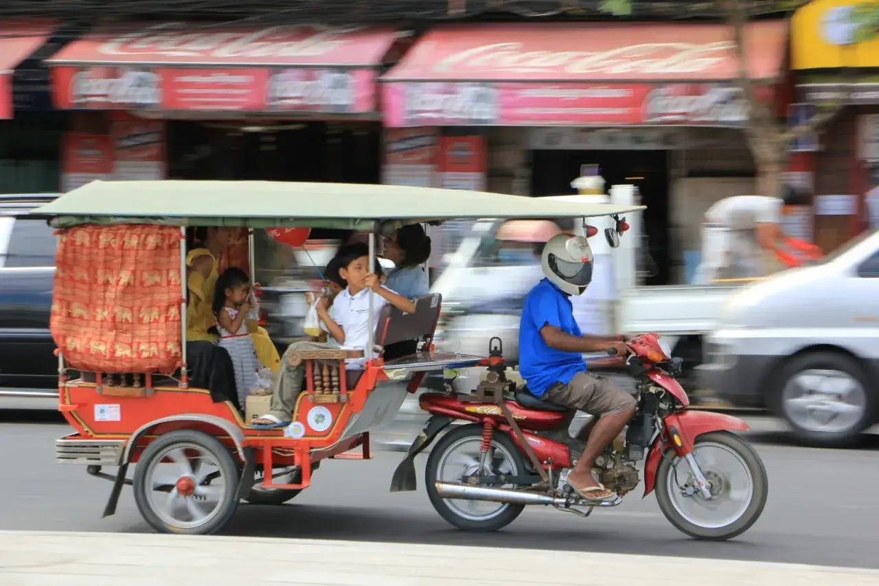 Rodzina w tuk-tuku, podr&oacute;żująca po ulicach Phnom Penh. Ceny w Kambodży są przystępne, co widać po możliwości podr&oacute;żowania taką formą transportu.