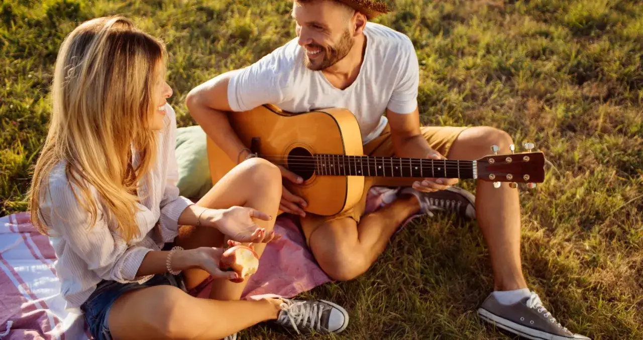 Ett par njuter av en picknick i solen. Mannen spelar gitarr medan kvinnan &auml;ter ett &auml;pple. Perfekta saker att hitta p&aring; med sin partner.