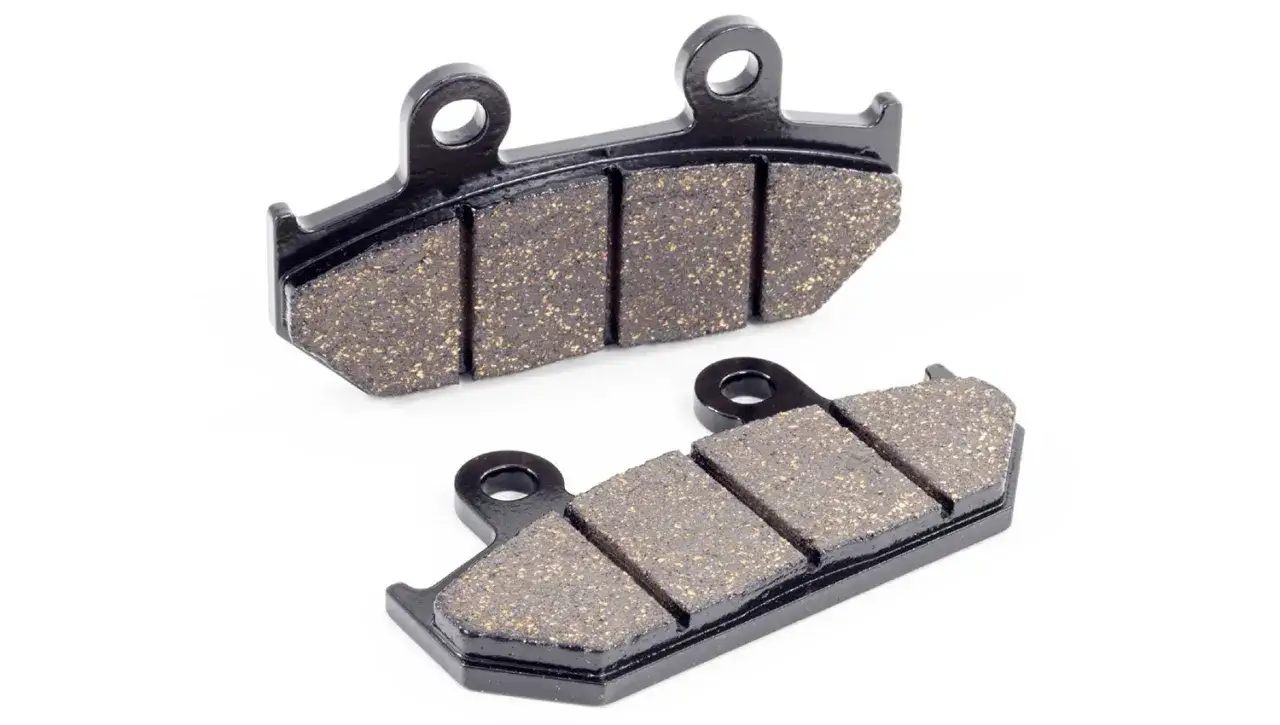Dos pastillas de freno de moto, con su superficie de fricción granulada y base metálica negra. Son esenciales para distintos tipos de pastillas de freno moto.
