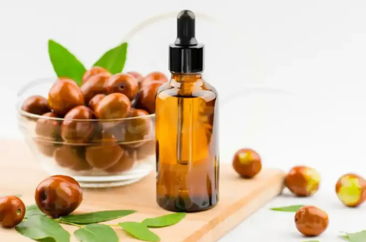 Bursztynowa buteleczka z pipetką i miseczka pełna owoców jojoby. Naturalny olej jojoba na włosy, który odżywi je i nada blasku.