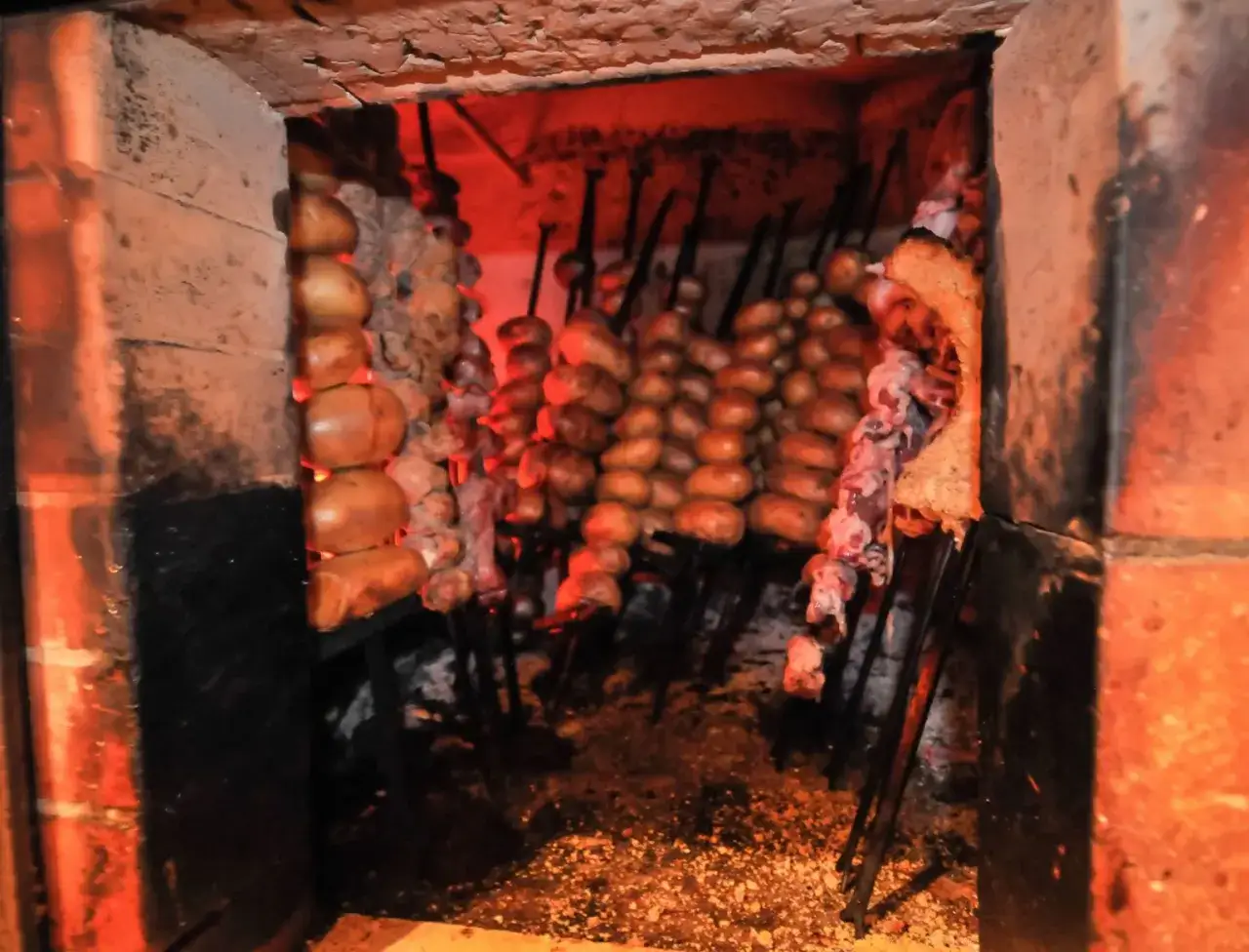 Spiedini di carne tipica pugliese e patate cuociono nel forno a legna, un'autentica delizia.