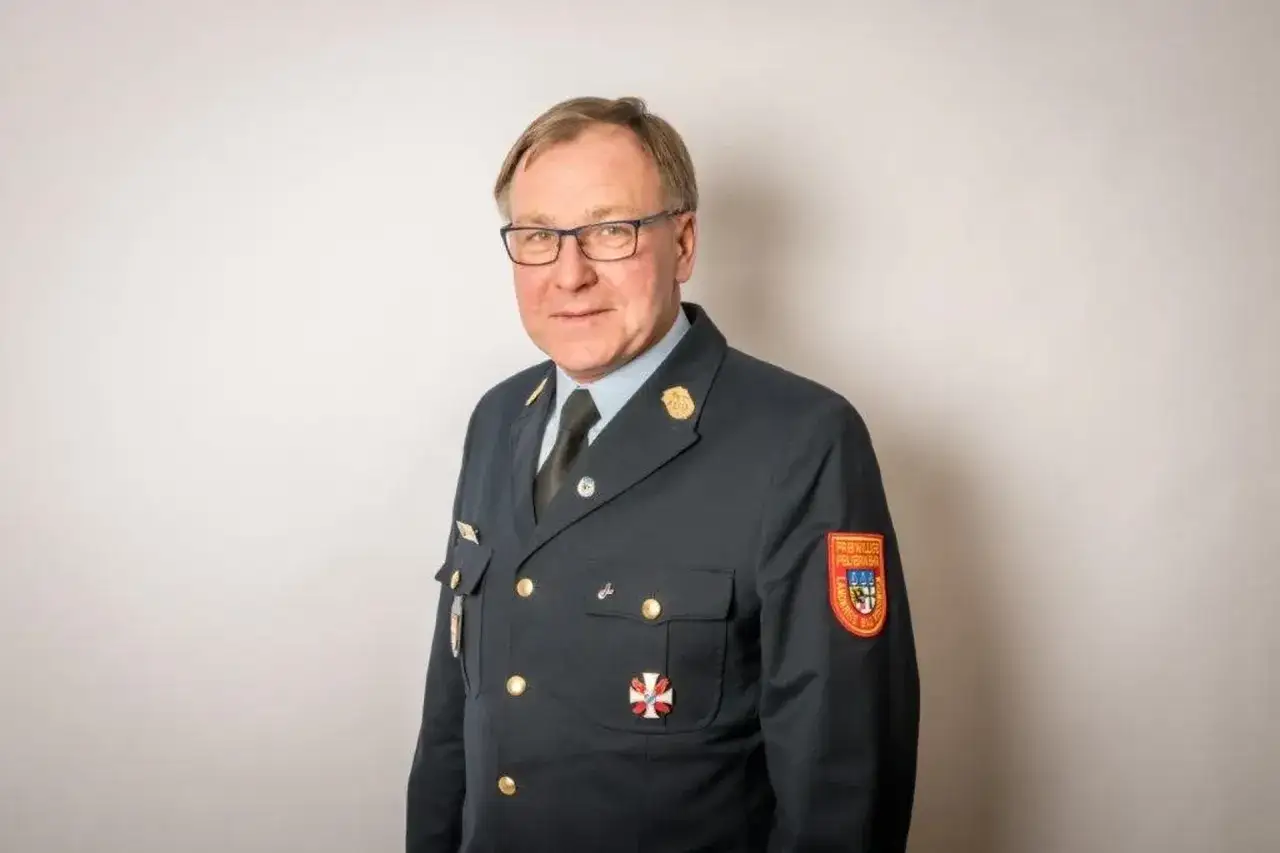 Mann in Uniform mit Feuerwehraufn&auml;her. Sein Kreisbrandrat Gehalt ist sicherlich angemessen f&uuml;r seine Verantwortung.