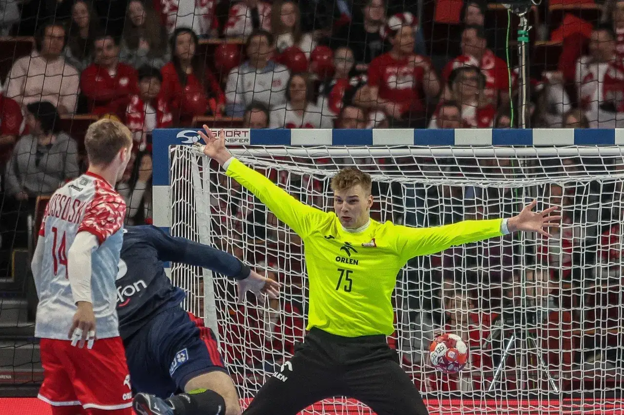 Bramkarz Sebastian Pieńkowski w neonowym stroju broni bramki. W tle kibice w biało-czerwonych barwach.