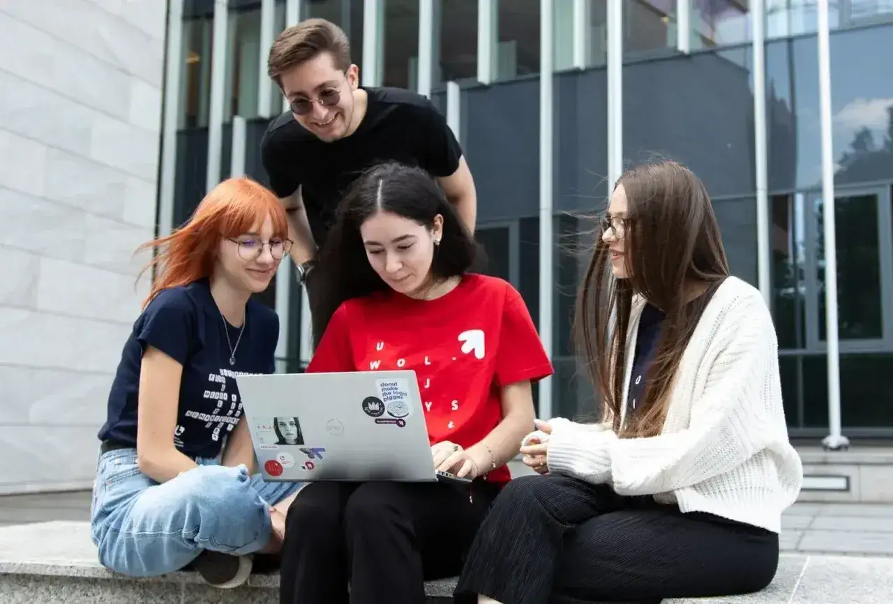 Studenci dyskutują o kierunkach na Uniwersytecie Łódzkim, przeglądając informacje na laptopie przed nowoczesnym budynkiem.