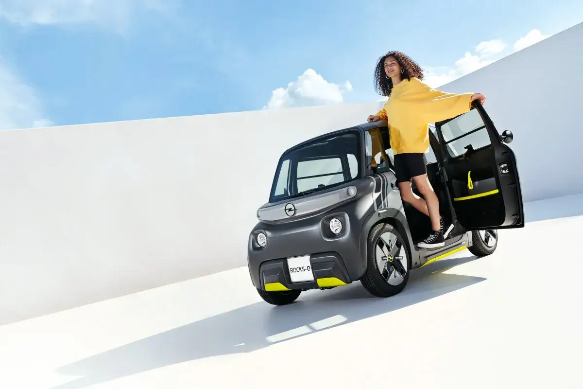 Młoda kobieta w żółtej bluzie wychodzi z miejskiego, opel elektryczny Rocks-e.