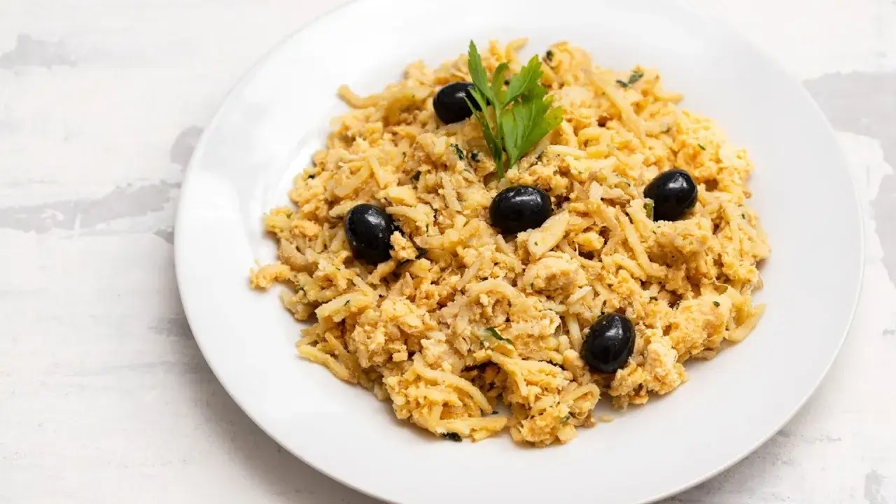 Delicioso bacalao a bras, un plato tradicional portugu&eacute;s, servido en un plato blanco con aceitunas negras y perejil.