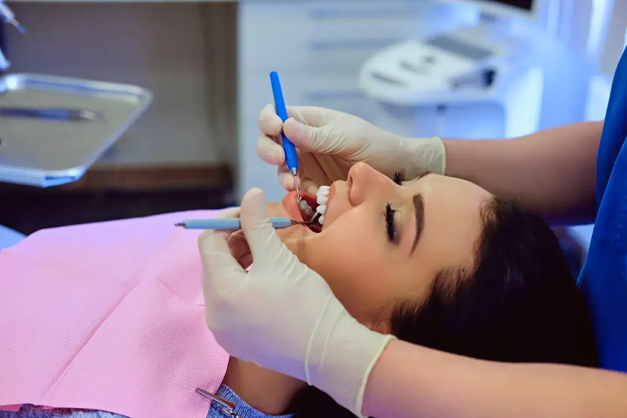 Dentysta aplikuje lekarstwo w zębie przed leczeniem kanałowym. Pacjentka leży na fotelu, z otwartymi ustami.