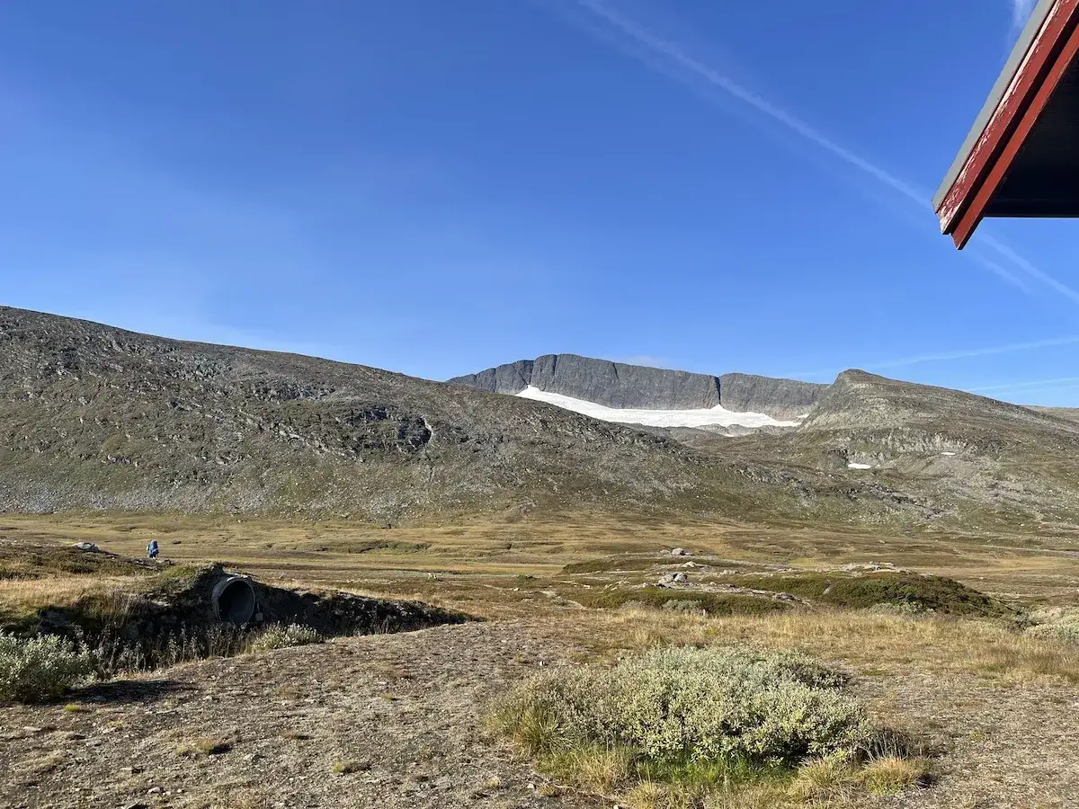 Vacker vy över fjällandskap med en glaciär på toppen, perfekt för att bestiga Helags. En ensam vandrare syns i fjärran.
