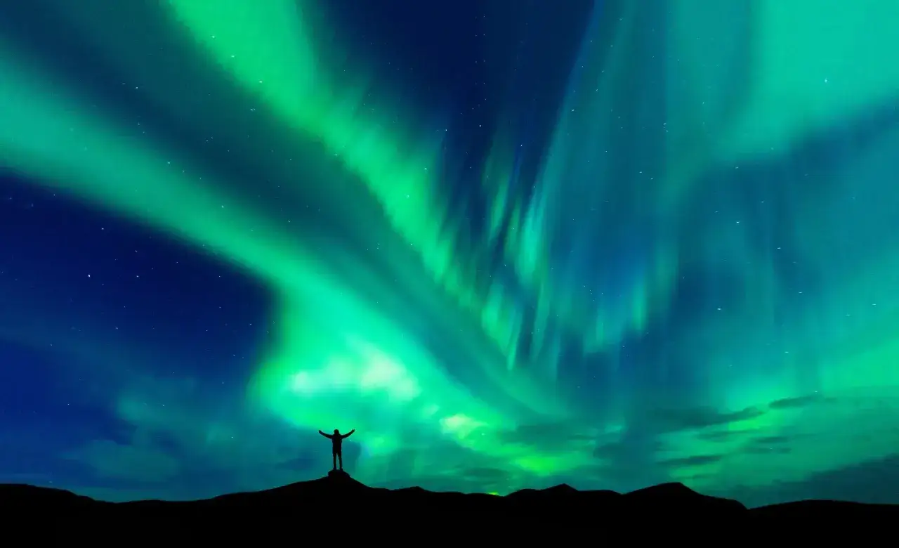En person står med armarna utsträckta mot ett magiskt kiruna norrsken som dansar över natthimlen.