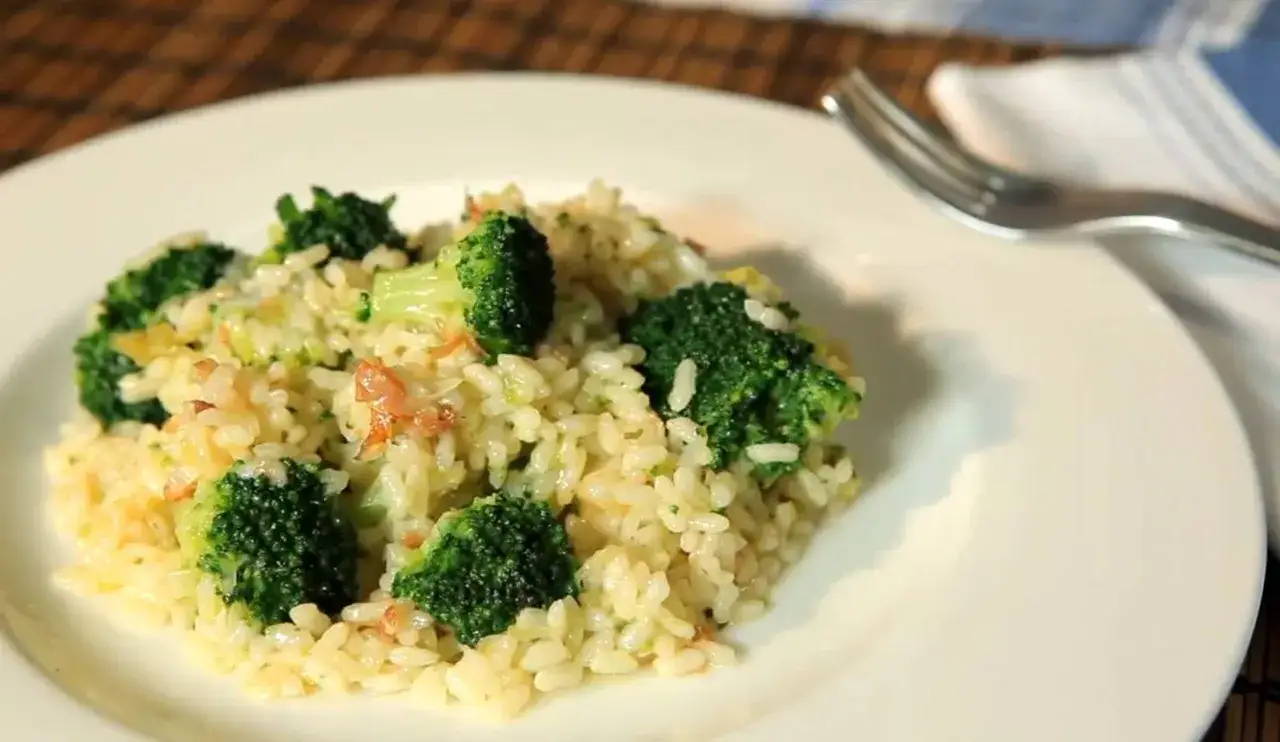 Delicioso arroz con br&oacute;coli cremoso, servido en un plato blanco con un tenedor a un lado.