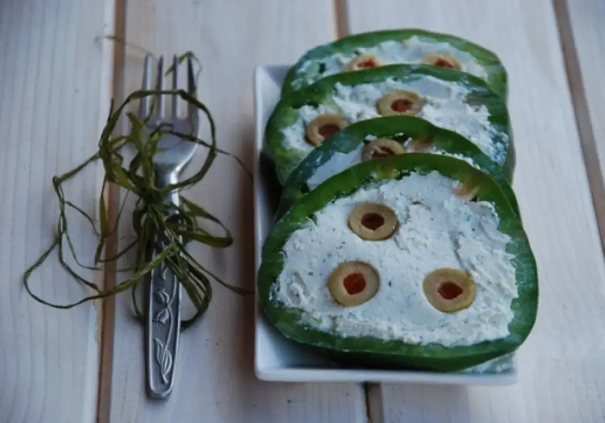 Kółka zielonej papryki nadziewane kremowym farszem z oliwkami. Obok widelec ozdobiony zieloną wstążką. Pyszna pasta z zielonej papryki.