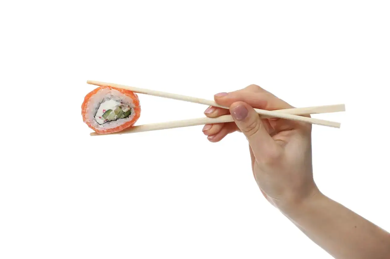 Dłoń trzyma pałeczkami sushi. Zobacz, jak łatwo można nauczyć się, jak używać pałeczek do sushi, by cieszyć się tym daniem.