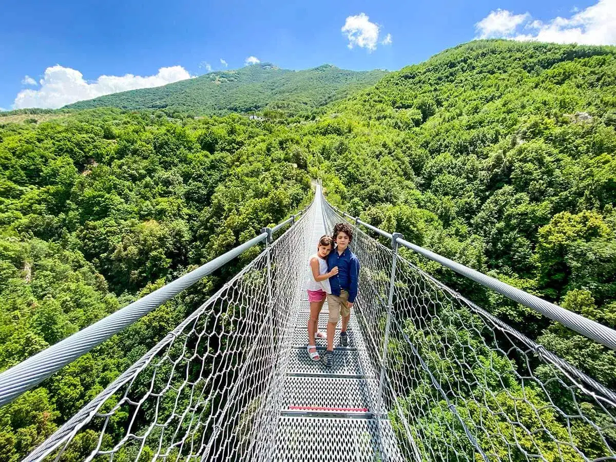 Bambini su un ponte tibetano nelle Marche, immersi nel verde lussureggiante delle colline. Un'avventura mozzafiato tra le montagne.