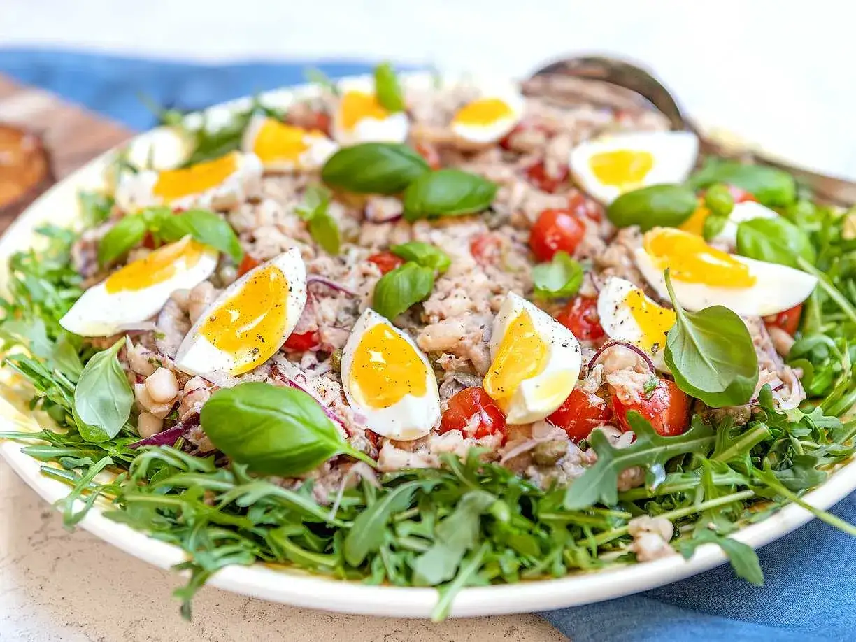 En härlig tonfisk sallad med ägg, tomater, bönor och basilika, serverad på en bädd av ruccola.