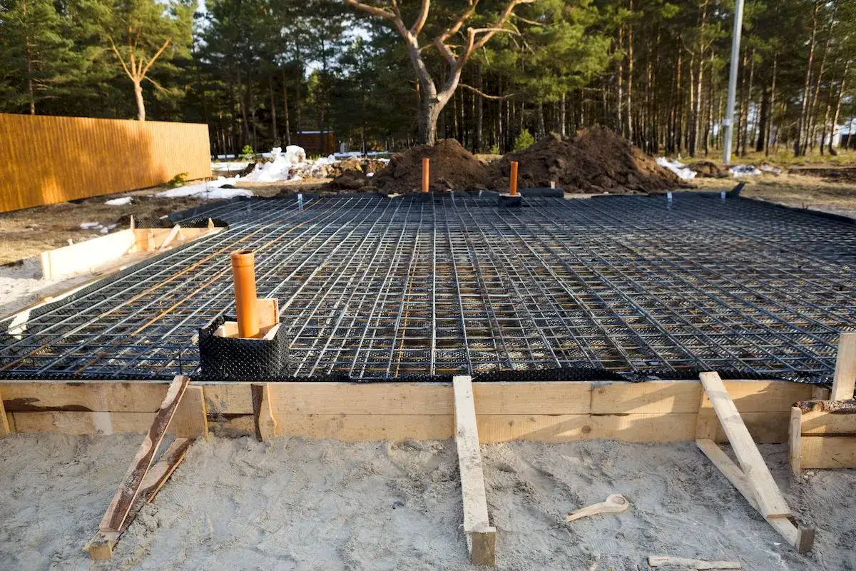 Siatka zbrojeniowa na fundamencie 100m2, przygotowana do wylania betonu. Widać drewniane szalunki i rury instalacyjne.