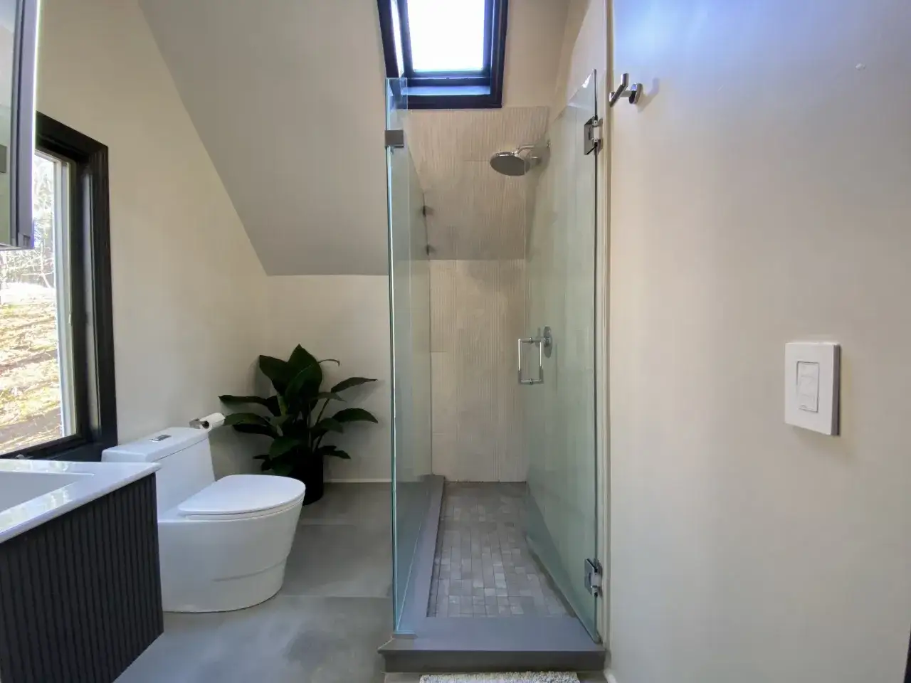 Modern bathroom with glass shower, toilet, and sink. This DIY bathroom remodel features a skylight and a large window.