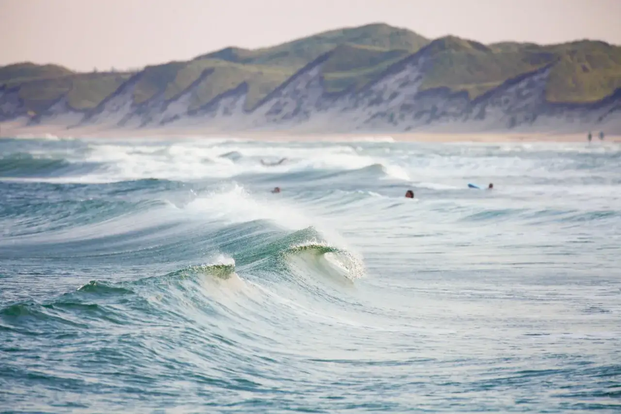 Wellen brechen sich am Strand von Klitmoller, Dänemark. Surfer warten auf die nächste Welle.