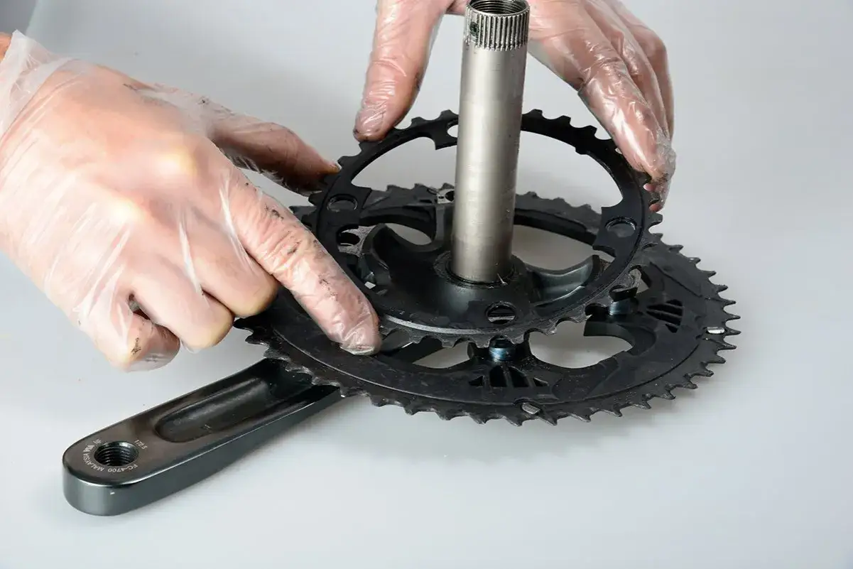 Händer med handskar monterar ett framdrev till en cykel.