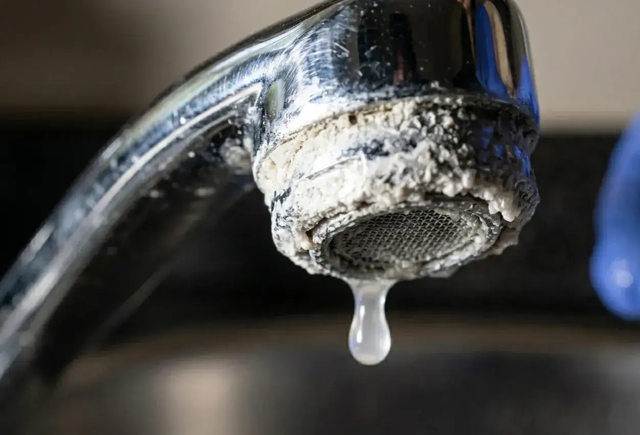 Goutte d'eau tombant d'un robinet qui goutte, couvert de calcaire. Un robinet qui goutte, un probl&egrave;me courant.
