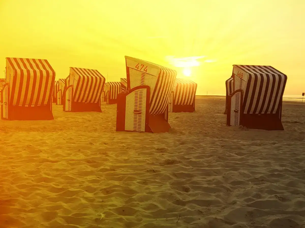 Zachód słońca na piaszczystej plaży na wyspach fryzyjskich w Niemczech. Rzędy charakterystycznych koszy plażowych w pasy czekają na plażowiczów.