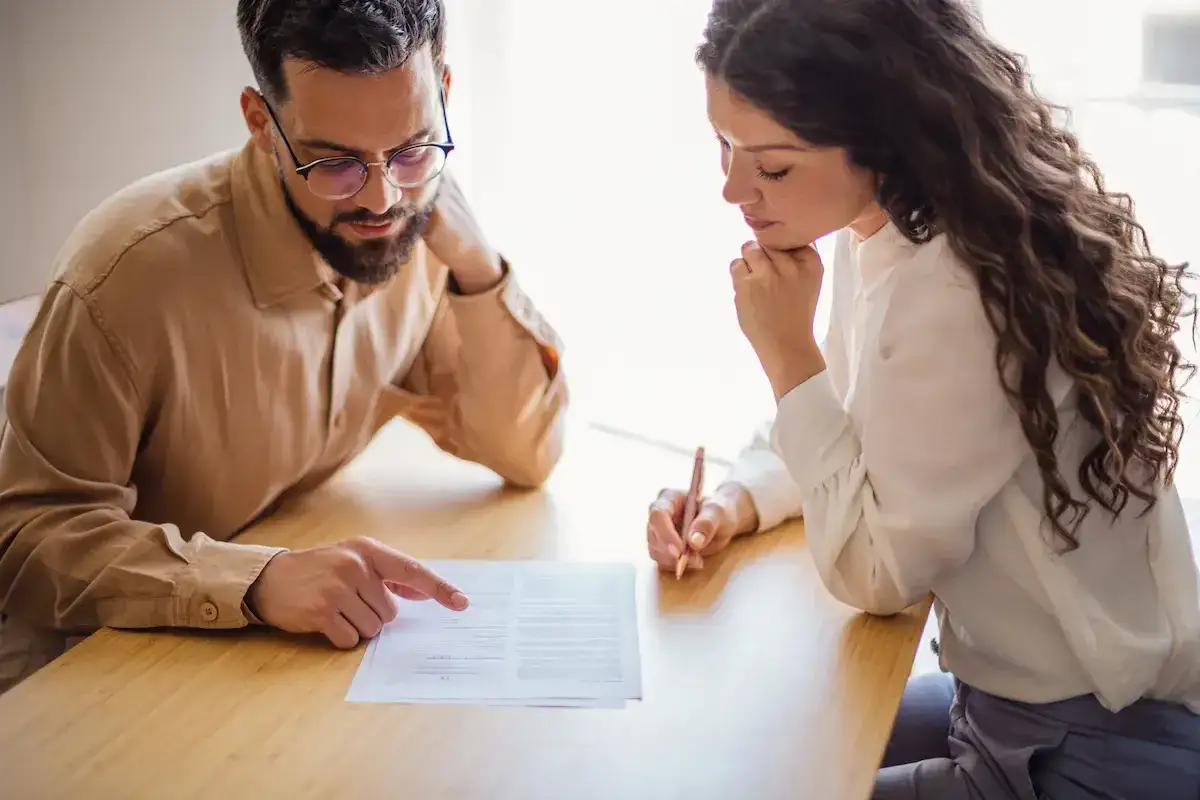 Hombre y mujer revisan un contrato. Él señala un punto, ella firma. Un momento clave en su comision inmobiliaria venta.