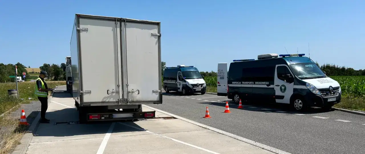 Inspektor sprawdza masę całkowitą ciężar&oacute;wki. Obok stoją furgonetki Inspekcji Transportu Drogowego.