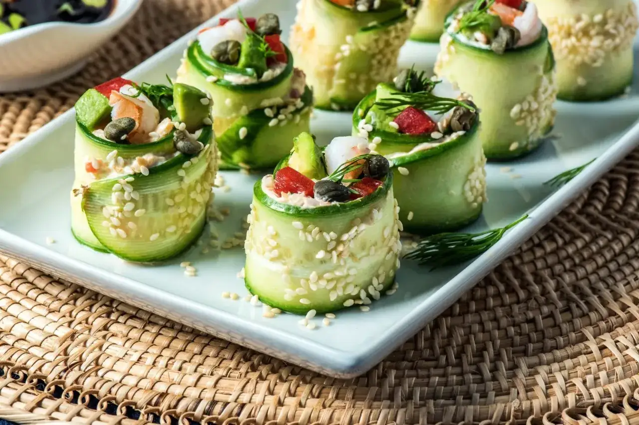 Erfrischende low carb sushi-Röllchen aus Gurke, gefüllt mit Garnelen, Avocado und Kapern, bestreut mit Sesam.