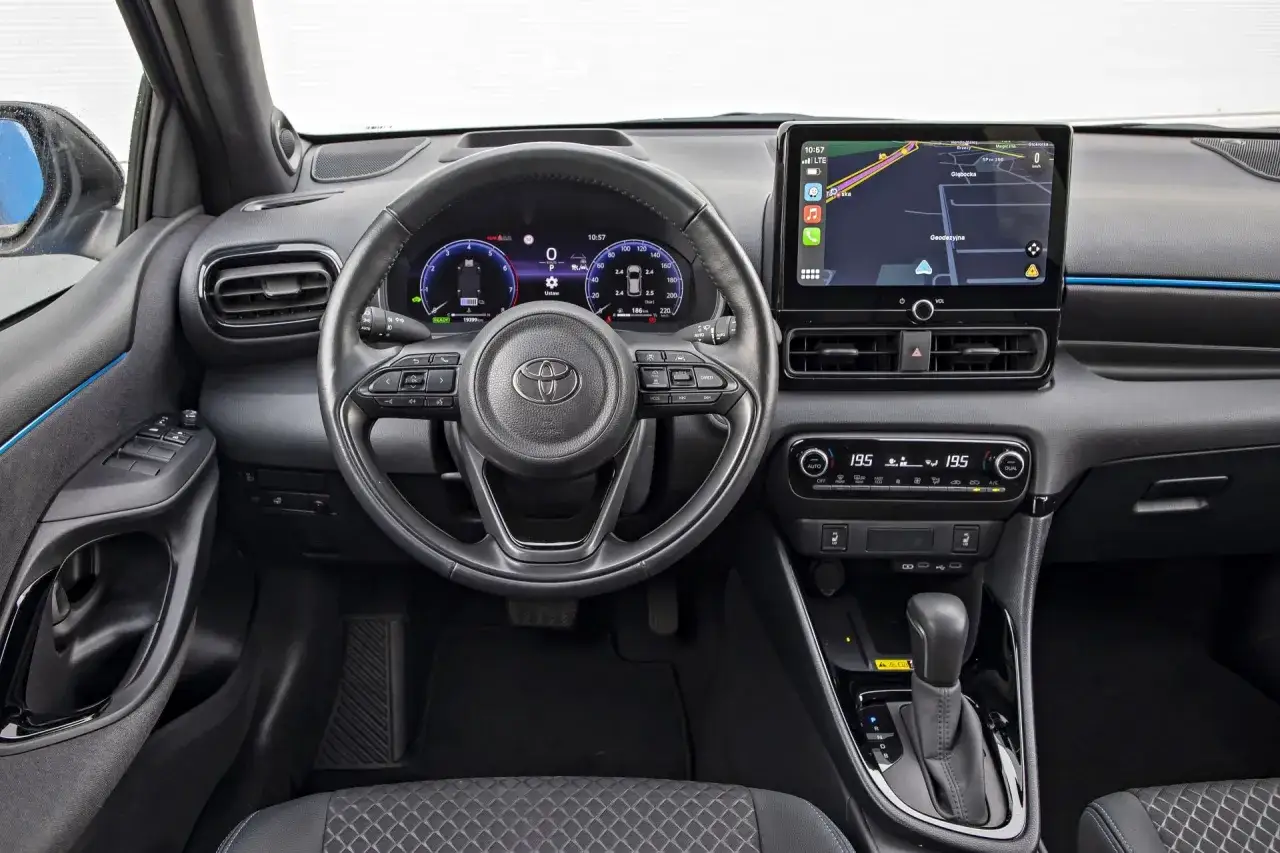Wnętrze Toyoty Yaris. Zobacz aktualne ceny i wyposażenie tego modelu. Kierownica, ekran nawigacji i panel klimatyzacji.