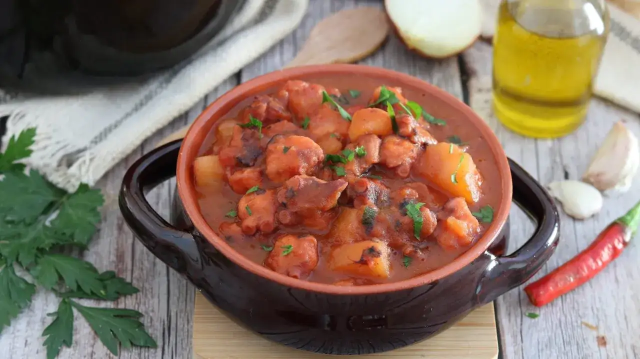 Un saporito polpo alla pignata, con patate e prezzemolo, servito in una ciotola di terracotta.