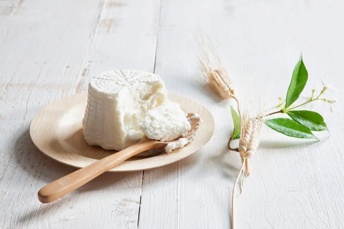 Świeża ricotta na drewnianym talerzyku, obok kłosy zbóż i gałązka jaśminu. Idealna do dań, gdy szukasz, czym zastąpić ricottę.