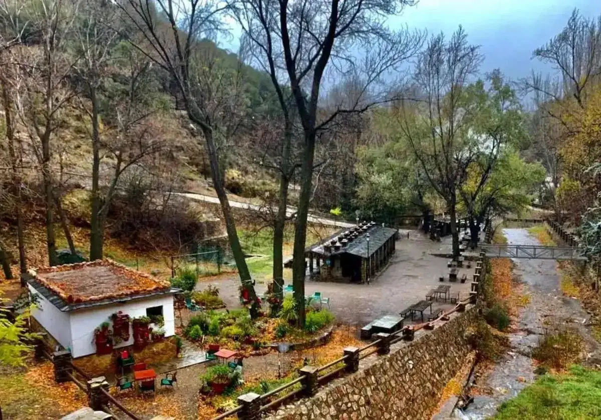 El merendero Laujar, un lugar acogedor en plena naturaleza, con un peque&ntilde;o edificio blanco y un restaurante alargado, rodeado de &aacute;rboles y un arroyo.