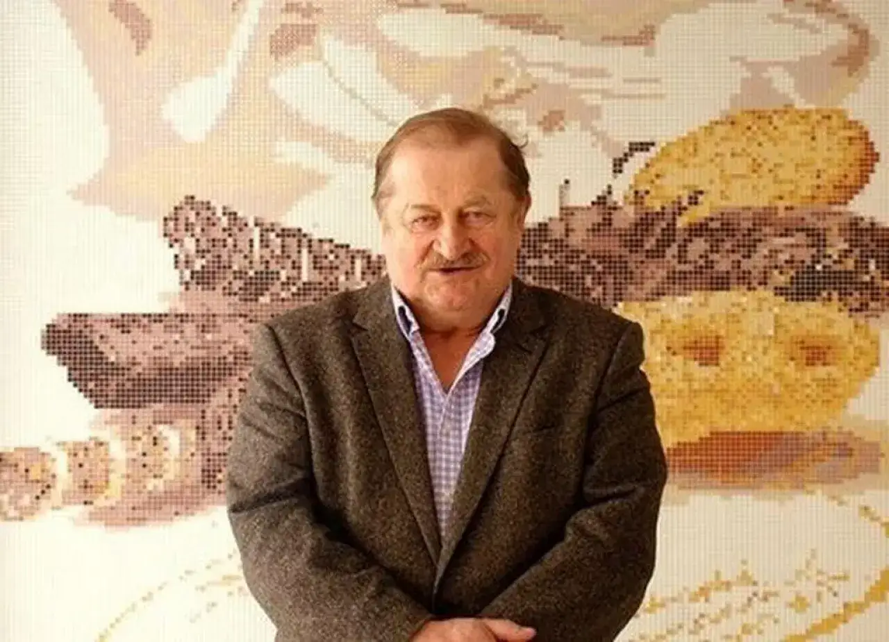 Jarosław Gołębiewski, znany jako Tago, pozuje przed mozaiką przedstawiającą abstrakcyjne kształty.