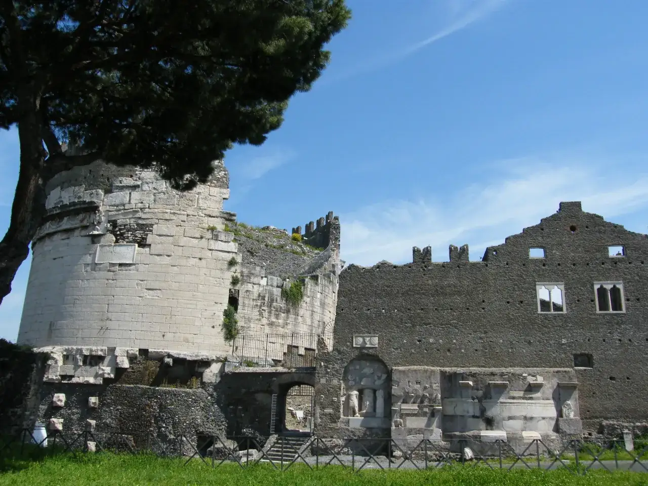Vestiges d'une ancienne demeure le long de la via Appia, avec une tour circulaire en pierre claire et une muraille sombre.